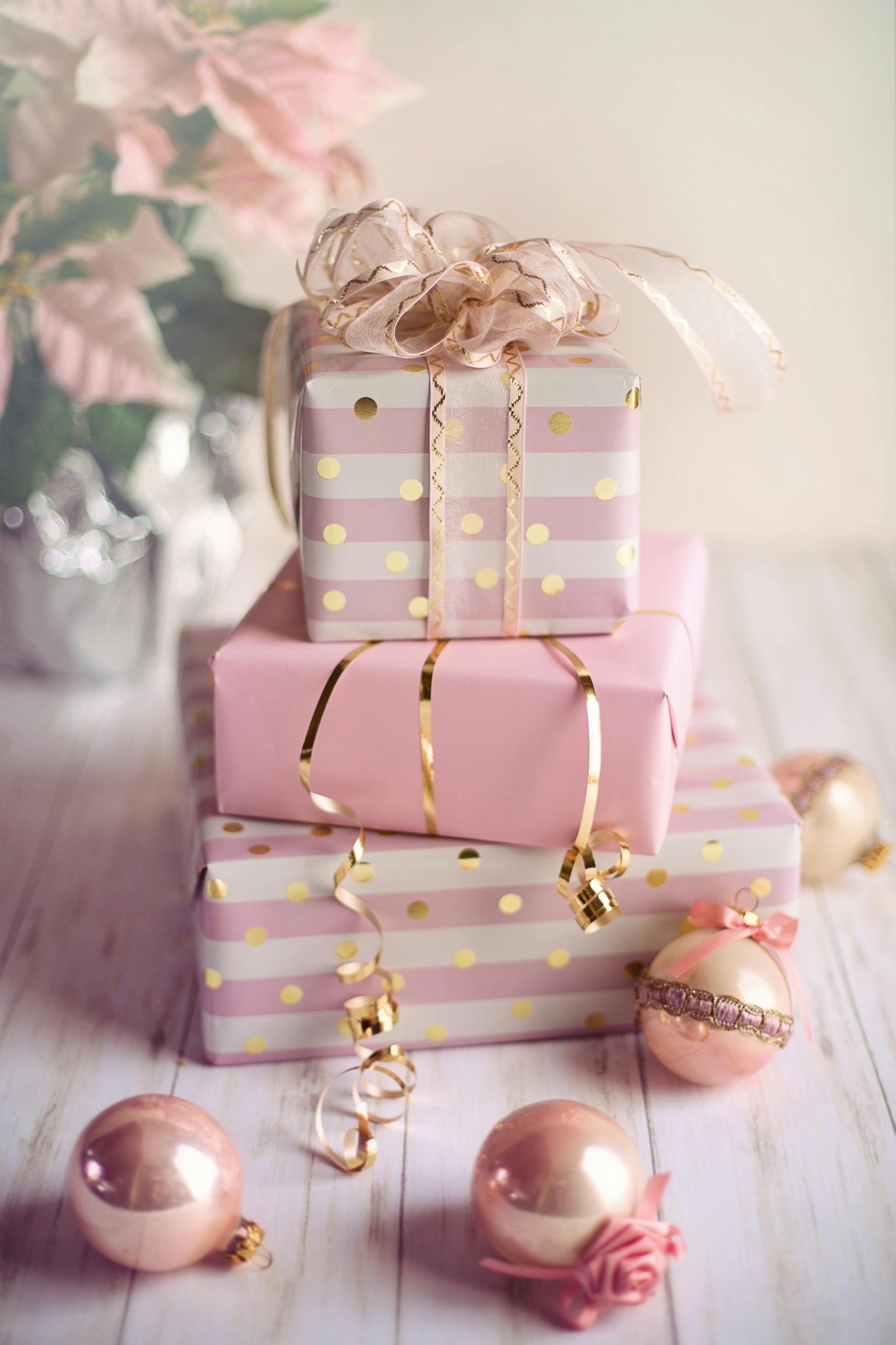 Charming Christmas presents wrapped in pink and gold with festive ornaments on a wooden table.