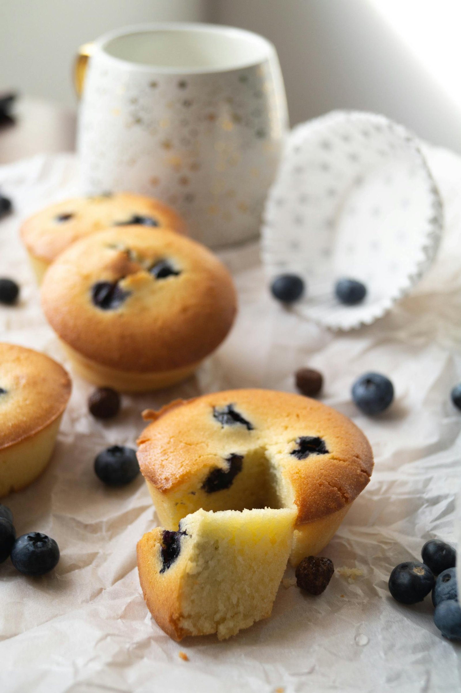 Freshly baked blueberry muffins with a coffee mug on a light background.